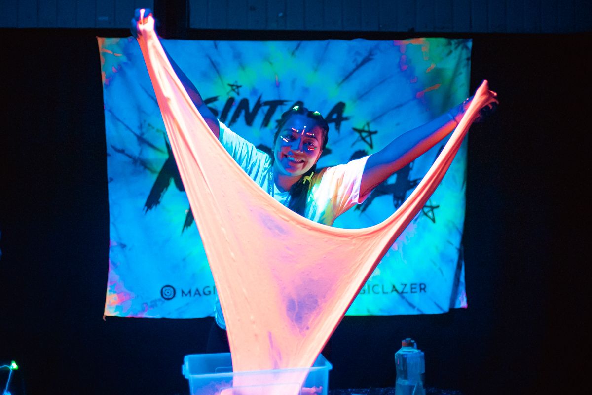 Victoria esticando slime gigante que brilha no escuro, em oficina Magic Lazer